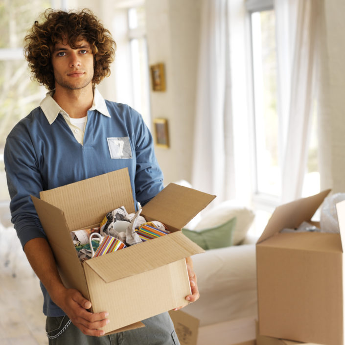 Portrait of a young man carrying mugs in a cardboard box